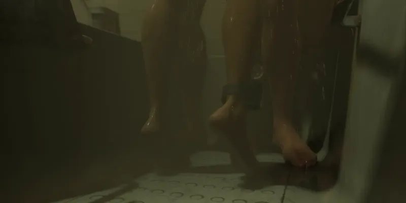 Eine Dusche, im Bild nur die Füße. Am Knöchel sitzt ein schwarzer Sender. Bild: Rockstar Games, Launch Trailer